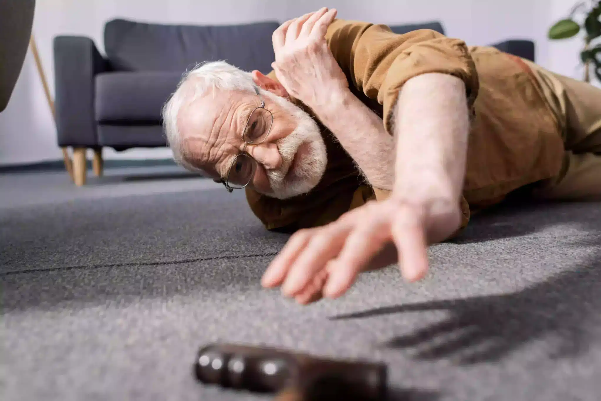 Elderly man falls on the ground stretching to pick up his walking stick